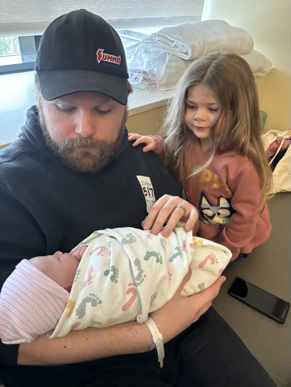Nathaniel holding his newborn with his daughter beside him